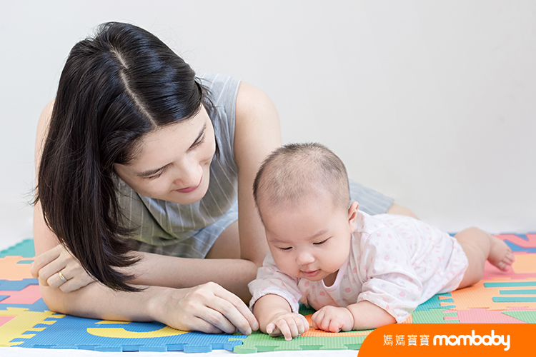 Mother playing with a little adorable newborn infant baby girl that lying on the tummy on colorful eva foam indoors